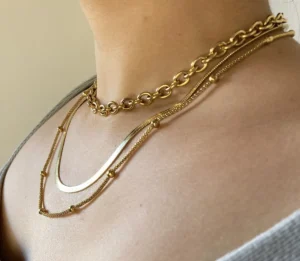 Look Layering Collares Dorados Vista lateral de una mujer usando el set de tres collares dorados de acero.