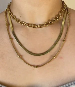 Detalle Set Collares Dorados en Piel Primer plano del pecho de una mujer mostrando el set de collares dorados en capas.