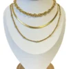 Set Collares Dorados Acero en Busto Set de tres collares dorados de acero quirúrgico exhibidos en un busto de joyería blanco.