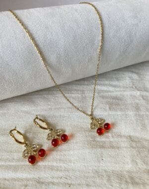 Portada Set Collar y Aros Cereza Set de joyas para mujer de acero dorado hipoalergénico, mostrando el collar y los aros con dijes de cereza sobre una tela de lino blanco.