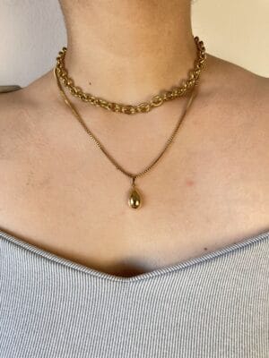 Combo Rustik y Dije Gota en Modelo (Frontal) Vista frontal de una modelo luciendo el set de dos collares de acero dorado: el choker Rustik y el collar con dije de gota, creando un efecto layering.