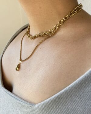 Set Collares Layering en Modelo (Perfil) Vista de perfil de una modelo usando el set de collares en capas Rustik-dropCuadros, destacando el brillo del acero dorado sobre la piel.