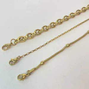 Detalle de Cierres de Acero Quirúrgico Primer plano de los tres cierres tipo mosquetón de los collares de acero dorado, mostrando la calidad y durabilidad del set de joyas para mujer.