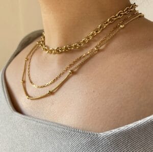 Look Completo con Set de Collares Layering Modelo usando el set de tres collares de acero dorado en capas, con una blusa de hombro descubierto, mostrando la versatilidad y elegancia del combo.