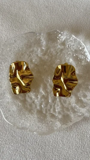 Brillo y Textura Aros Dorados Par de aros chunky dorados sobre un plato de vidrio texturizado.