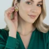 Aros Dorados en Uso Mujer rubia colocándose un aro chunky dorado en la oreja.