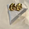 Diseño Artístico Aros Dorados Aros chunky dorados con diseño molten sobre una figura geométrica blanca.