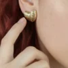 Aro Corazón en Modelo Primer plano del aro de corazón dorado en la oreja de una modelo pelirroja.
