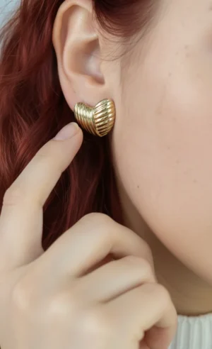Aro Corazón en Modelo Primer plano del aro de corazón dorado en la oreja de una modelo pelirroja.