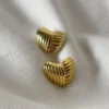 Aros Corazón Acero Quirúrgico Par de aros de corazón dorados de acero quirúrgico sobre tela blanca.
