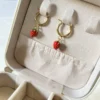 Guardá tus Aros Coquette Vista superior de los aros de frutilla dorados colocados en las ranuras de un joyero.