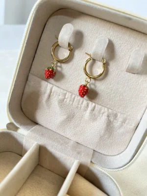 Guardá tus Aros Coquette Vista superior de los aros de frutilla dorados colocados en las ranuras de un joyero.
