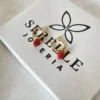 Aros Frutilla Dorados Serelle Par de aros de frutilla dorados sobre la caja de regalo blanca de Serelle Joyería.