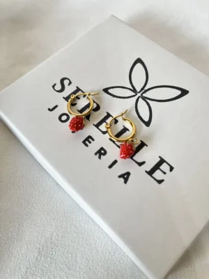 Aros Frutilla Dorados Serelle Par de aros de frutilla dorados sobre la caja de regalo blanca de Serelle Joyería.