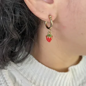 Aros Frutilla Coquette en Oreja Primer plano de una mujer usando un aro de argollita dorada con un dije de frutilla roja.