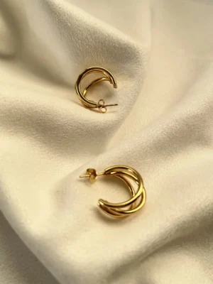 Diseño Entrelazado Aros Triple Argolla Par de aros de triple argolla dorada entrelazados sobre una superficie blanca.