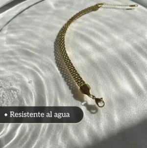 Joya de Acero Resistente al Agua Pulsera de acero quirúrgico dorado sobre una superficie de agua para demostrar su resistencia.