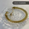 Pulsera Dorada de Malla Plana - Vista Completa Pulsera de acero inoxidable dorado con tejido de malla plana sobre una base de cristal.