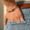Look Casual con Pulsera Dorada Detalle de la muñeca de una mujer con la pulsera de tréboles, con la mano en el bolsillo de un jean.