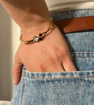 Look Casual con Pulsera Dorada Detalle de la muñeca de una mujer con la pulsera de tréboles, con la mano en el bolsillo de un jean.