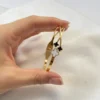 Perfil del Diseño Cruzado de la Pulsera Mano de una mujer sosteniendo la pulsera de perfil, mostrando el diseño cruzado de la esclava.