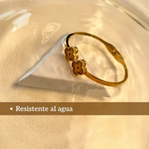 Pulsera Resistente al Agua Pulsera dorada de tréboles, resistente al agua, sobre una base blanca.